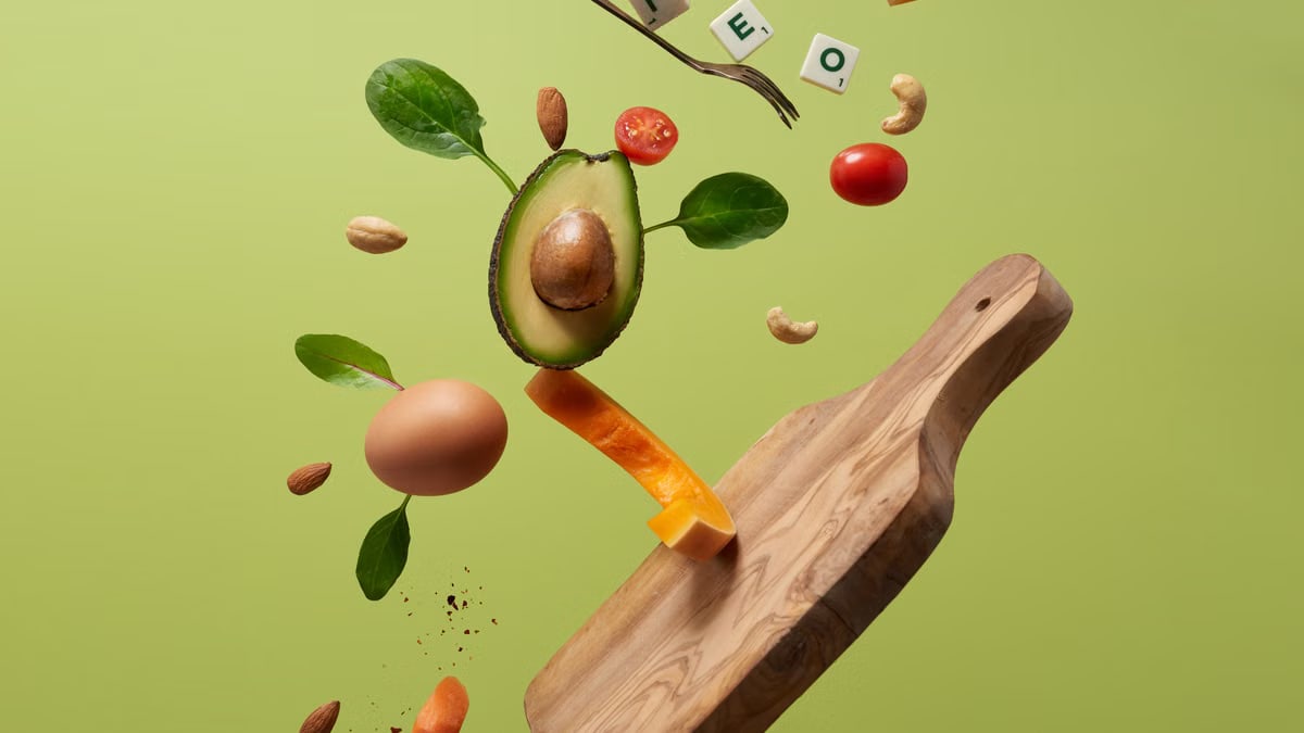 A creative arrangement of paleo diet ingredients floating above a wooden board on a green background.
